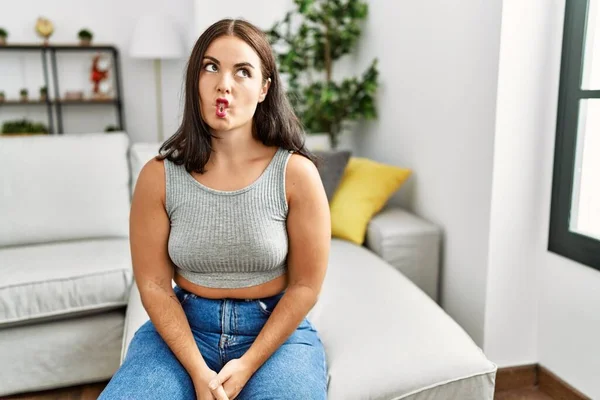 Evdeki kanepede oturan genç esmer kadın dudaklarıyla balık suratı yapıyor, çılgınca ve komik bir jest. Komik ifade. 