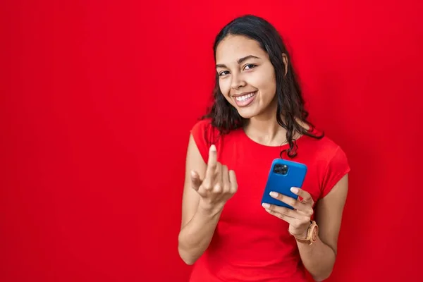 年轻的巴西女人在红色背景下用智能手机招呼客人 手拉着欢迎快乐微笑来到这里 — 图库照片