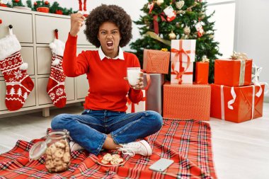 Afro saçlı genç Afrikalı bir kadın noel ağacında oturmuş hamur işi yiyor öfkeyle bağırıyor, öfkeyle çılgınca bağırıyor ve el kaldırıyor. 