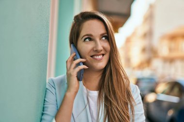 Genç sarışın iş kadını gülümsüyor. Şehirdeki akıllı telefondan konuşuyor..