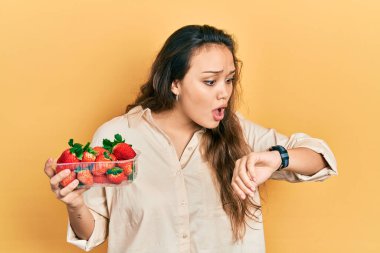 Çilek tutan genç İspanyol kız saate bakıyor. Endişeli, geç kalmaktan korkuyor. 