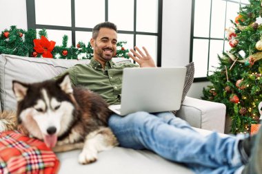 Genç İspanyol adamın evdeki Noel ağacının yanında köpekle kanepede otururken görüntülü konuşması var.