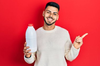 Sakallı, elinde litrelik süt şişesi olan genç İspanyol adam mutlu bir şekilde elini ve parmağını kenarı işaret ediyor. 