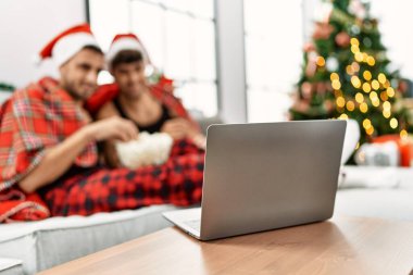 Evde Noel ağacının yanında oturmuş film izleyen iki İspanyol erkek.