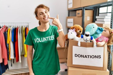 Bağışlarda gönüllü tişört giyen güzel beyaz kadın gülümseyip, parmaklarını ve ağzını göstererek gülümsüyor. diş sağlığı kavramı. 