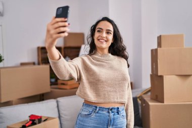 Genç İspanyol kadın yeni evindeki akıllı telefonun yanında selfie çekiyor.
