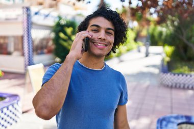 Genç İspanyol adam gülümsüyor. Parktaki akıllı telefondan konuşuyor.
