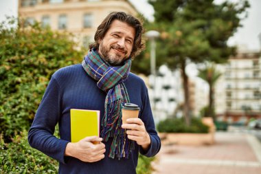 Orta yaşlı yakışıklı bir adam parkta bir fincan kahve içiyor.