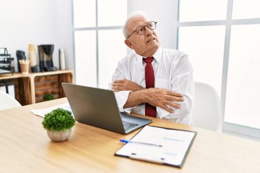 Ofiste çalışan kıdemli bir adam bilgisayar kullanıyor. Kolları çapraz ve kendinden emin bir şekilde yan tarafa bakıyor. 