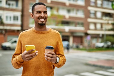 Genç Afrikalı Amerikalı adam akıllı telefon kullanıyor. Şehirde kahve içiyor..
