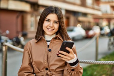 Genç, güzel esmer kadın dışarıda mutlu bir şekilde gülümsüyor akıllı telefon kullanıyor.