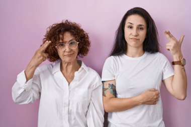 İspanyol anne ve kızı pembe arka plan üzerine gündelik beyaz tişört giyip, silah gibi el ve parmakları işaret ederek, intihar jesti yaparak intihar ediyorlar.. 