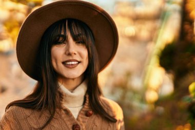 Parkta gülümseyen, kışlık şapkalı esmer kadın.