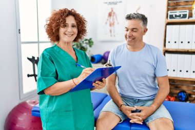 Orta yaşlı erkek ve kadın fizyoterapi üniforması giyip fizik tedavi kliniğinde rehabilitasyon seansı yapıyorlar.