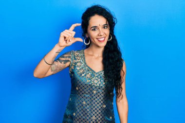 Bindi ve geleneksel kurta elbisesi giyen genç bir kadın gülümsüyor ve kendine güveni tam el hareketi yapıyor. Küçük boy işareti yapıyor, parmaklarına bakıyor ve kameraya bakıyor. ölçüm kavramı. 