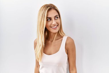 Sarışın, güzel, genç bir kadın beyaz, soyutlanmış arka planda duruyor. Yüzünde gülümseme, doğal bir ifade ile yan yana bakıyor. Kendinden emin gülen. 