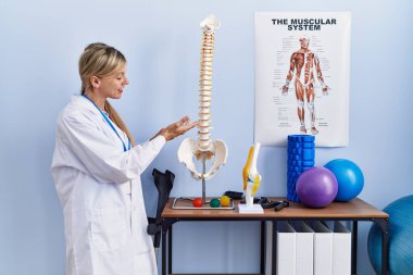 Fizyoterapi kliniğindeki omurganın anatomik modelini gösteren fizyoterpist üniforma giyen genç sarışın kadın.