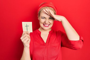 Elinde katolik haç tutan genç sarışın kadın. Elleri başının üstünde, şaşırmış ve kızgın bir yüzle stresli ve hayal kırıklığına uğramış. 