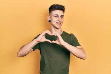 Kulakları genişlemiş, sıradan yeşil tişörtler giyen, aşkla gülümseyen, kalp sembolü ve elleriyle şekil veren beyaz bir çocuk. romantik kavram. 