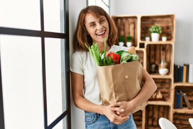 Beyaz kadın gülümsüyor. Elinde alışveriş poşeti var.