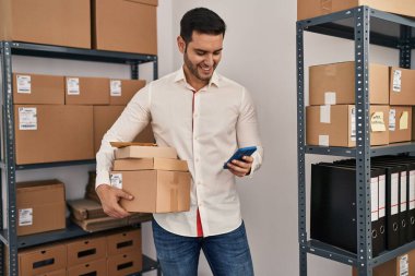 Genç İspanyol bir e-ticaret işçisi ofisteki akıllı telefon paketlerini kullanıyor.