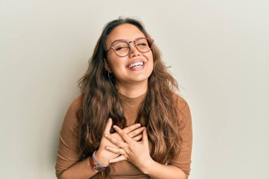 Gündelik kıyafetler ve gözlük takan genç İspanyol kız elleri göğsünde, gözleri kapalı ve yüzünde minnet dolu bir jest ile gülümsüyor. sağlık kavramı. 