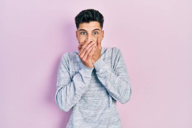 Gündelik kıyafetler giyen genç İspanyol adam yanlışlıkla elleri ile ağzını kapatırken şok oldu. gizli kavram. 