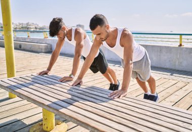 Two hispanic men couple stretching at seaside