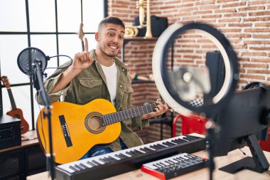 Latin asıllı genç bir adam online gitar dersi veriyor. Bir fikir veya soru işareti ile gülümsüyor. Bir numara: 