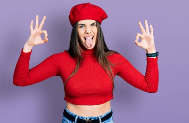 Young brunette teenager doing excellent gesture with hand sticking tongue out happy with funny expression. 