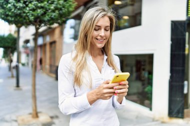 Güneşli bir günde gülümseyen güzel sarışın kadın akıllı telefon kullanıyor.