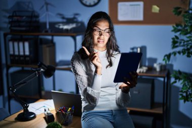 Geceleri dokunmatik ped kullanan genç Brezilyalı bir kadın ofiste çalışıyor. Endişeli ve endişeli bir ifade takınıyor. 