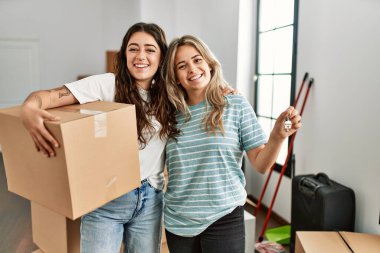 Mutlu bir şekilde gülümseyen genç çift yeni evin anahtarını ve karton kutuyu tutuyor..