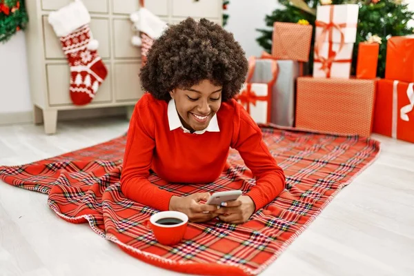 Young African American Woman Using Smartphone Lying Christmas Tree Home — Fotografia de Stock