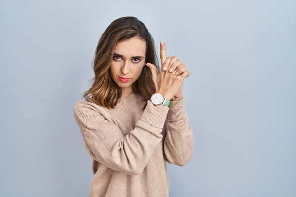 Young woman standing over isolated background holding symbolic gun with hand gesture, playing killing shooting weapons, angry face