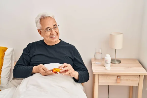 Senior man taking pills treatment sitting on bed at bedroom