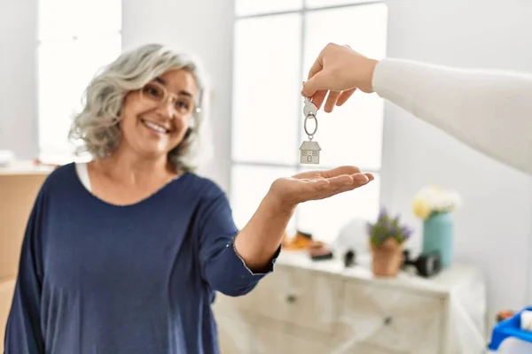 Middle age grey-haired woman smiling happy holding key of new home.