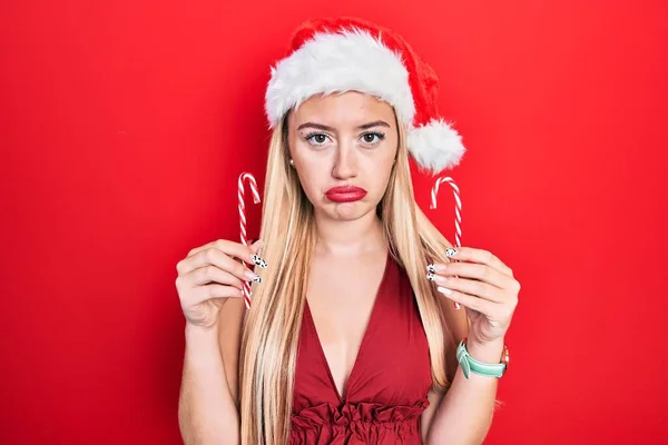 クリスマスの帽子をかぶっている若いブロンドの女の子は キャンディを持って落ち込んでおり 苦痛を心配し 怒って恐れています 悲しい表情 — ストック写真