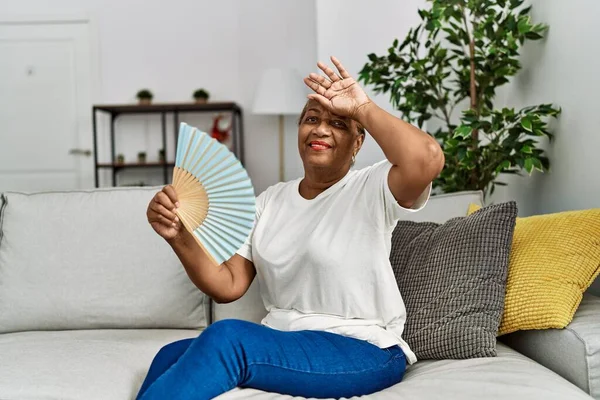 Ανώτερη Αφροαμερικανή Γυναίκα Που Χρησιμοποιεί Ανεμιστήρα Χειρός Κάθεται Στον Καναπέ — Φωτογραφία Αρχείου