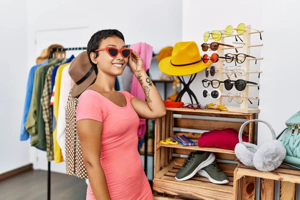 Young hispanic woman customer smiling confident wearing sunglasses at clothing store