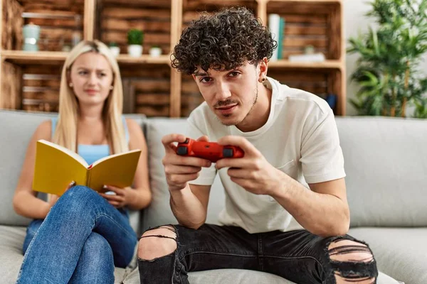 Casal Jovem Com Expressão Séria Jogando Videogame Lendo Livro Casa — Fotografia de Stock