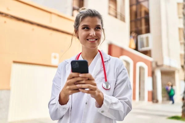 年轻的金发女人穿着医生制服 在街上用智能手机 — 图库照片