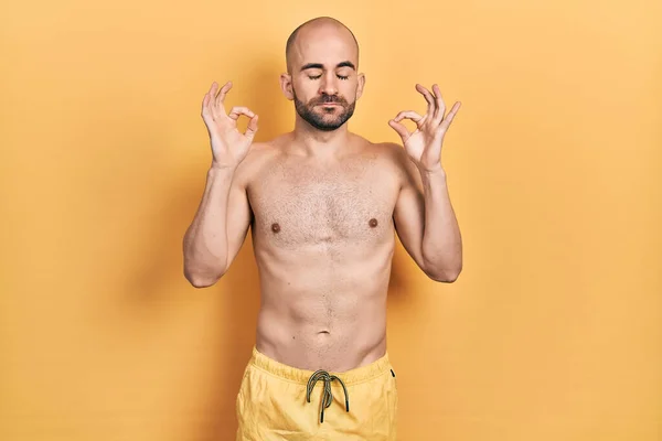 Young bald man wearing swimwear relax and smiling with eyes closed doing meditation gesture with fingers. yoga concept.