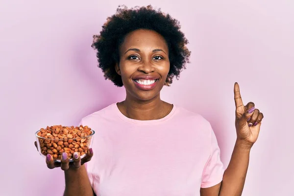 若いアフリカ系アメリカ人の女性は 幸せな顔をしたアイデアや質問を指差す指で笑顔でピーナッツを保持 ナンバーワン — ストック写真