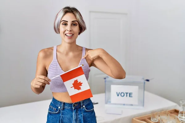 Young beautiful woman at political campaign election holding canada flag pointing finger to one self smiling happy and proud