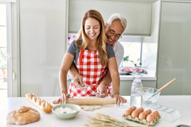 Orta yaşlı İspanyol çift mutlu gülümsüyor ve mutfakta hamur yoğuruyorlar..