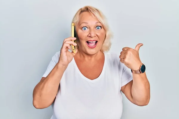 Middle Age Blonde Woman Having Conversation Talking Smartphone Pointing Thumb — Foto de Stock