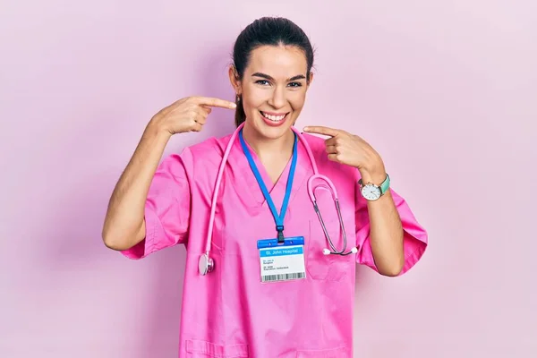 Doktor Üniforması Giyen Genç Esmer Kadın Steteskop Gülümseyen Parmaklarıyla Ağzıyla — Stok fotoğraf