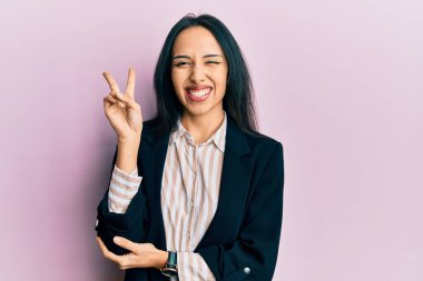 İş kıyafetleri giymiş, gülümseyen ve kameraya göz kırpan genç İspanyol kız zafer işareti yapıyor. İki numara.. 