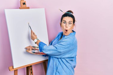 Genç İspanyol kadın resim sehpası boyunca paletle resim çiziyor. Korkuyor ve şaşkınlık içinde, şaşkınlık içinde, şaşkınlık içinde duruyor.. 